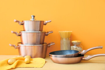Set of copper kitchen utensils with raw food on table against orange background