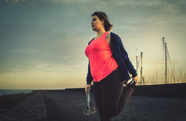 Young chubby woman sport workout on the harbor bridge stretching legs - healthy concept of curvy...