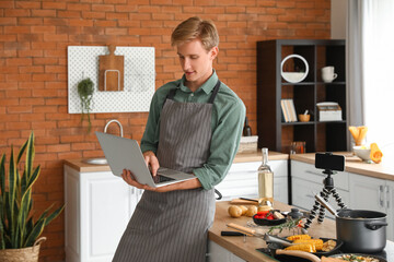 Handsome young man using laptop while cooking in kitchen