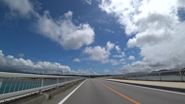 OKINAWA, JAPAN - AUG 2021 : Driving around Kouri Island bridge in sunny summer day. Wide camera, point of view (POV), seaside road driving. Holiday, vacation and resort concept.