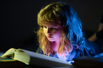 Happy childhood, dreaming child. A little cute boy reading a book lying on the bed. Child reading a...