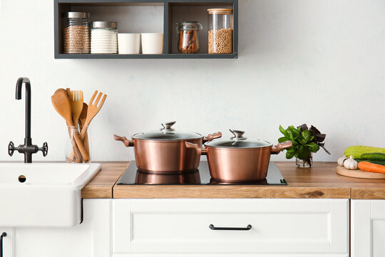 Shiny cooking pots on stove near light wall in kitchen