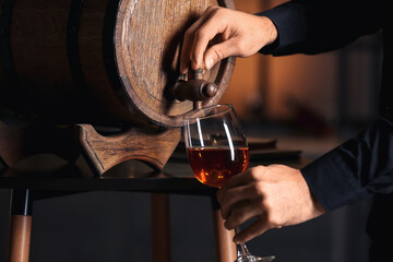 Young male sommelier pouring wine from barrel into glass, closeup