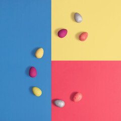 Easter eggs lay down on a multicolored geometric background. Square flat lay composition, minimal Easter celebration concept