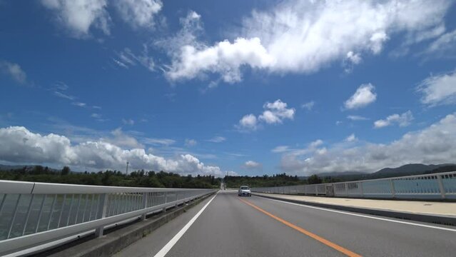 OKINAWA, JAPAN - AUG 2021 : Driving around Kouri Island bridge in sunny summer day. Wide camera, point of view (POV), seaside road driving. Time lapse shot. Holiday, vacation and resort concept.