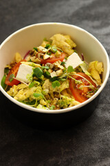 Bowl with scramble, feta cheese, tomatoes, walnuts and microgreens on a dark background in an eco paper box. Healthy food delivery concept.