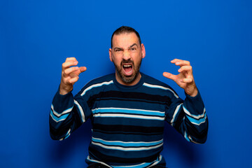 Bearded hispanic man wearing striped sweater pissed off and furious making cat claw gesture...