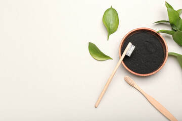 Bowl with activated charcoal tooth powder and toothbrushes on white background