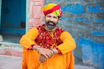 Portrait of happy traditional north indian man wearing colorful attire sitting. Smiling Rajasthan male with turban and ethnic outfits. Culture and fashion. looking at camera