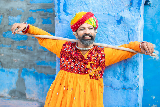 Happy traditional north indian man wearing colorful attire holding wood stick. Rajasthan male with turban and ethnic outfits. Culture and fashion.