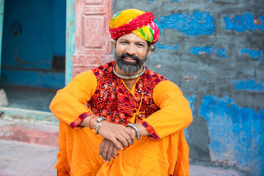 Portrait of happy traditional north indian man wearing colorful attire sitting. Smiling Rajasthan male with turban and ethnic outfits. Culture and fashion. looking at camera