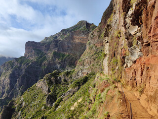Beautiful mountain landscape view with vibrant colors during a cloudy day with sun. Stripes on the rocks. Hiking trail with secured path. Travel the world. Nomad life. Adventurous lifestyle. 
