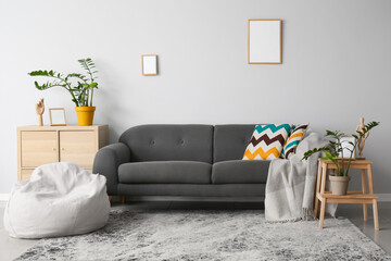 Comfortable sofa, houseplants and pouf near light wall