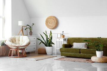 Comfortable sofa, houseplants and pouf near white wall in room
