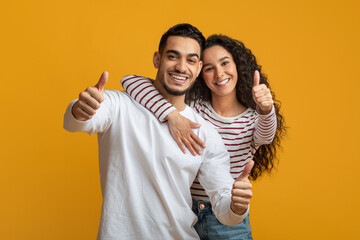 We Recommend. Cheerful Young Arab Spouses Showing Thumbs Up At Camera