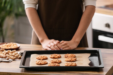Obraz na płótnie Canvas Woman with baking sheet of tasty peanut cookies at kitchen table, closeup