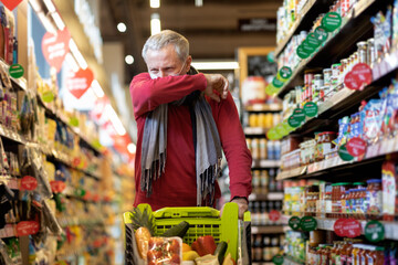 Sick elderly man in face mask posing with shopping cart