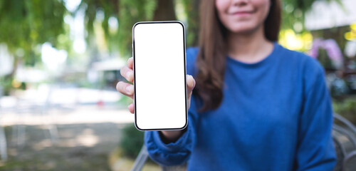 Mockup image of a young asian woman holding and showing a mobile phone with blank white screen