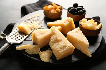 Wooden board with pieces of tasty Parmesan cheese on black background