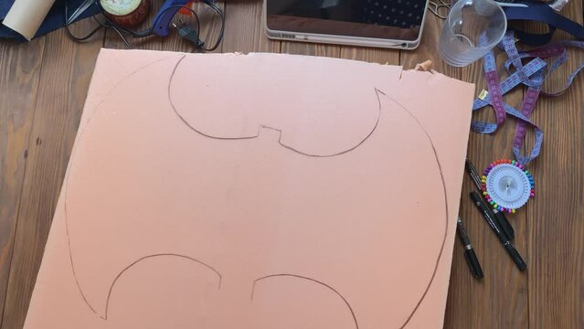 Woman removes craft paper from styrofoam. Silhouette of Celtic axe is drawn on foamed polyethylene. Viking hatchet on wooden table. Cosplayer workshop. Create weapons for festival of Middle Ages.