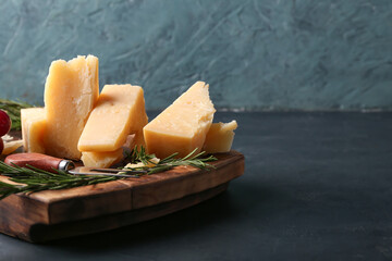 Wooden board with pieces of tasty Parmesan cheese on table