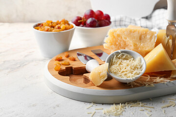 Wooden board with pieces of tasty Parmesan cheese on light background