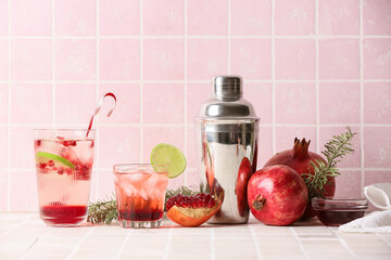 Glasses of tasty pomegranate cocktail, shaker and fruits on tile background