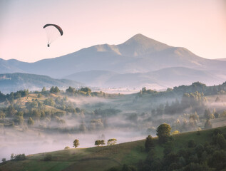 Paraglider flying above the misty carpathian hills - 490032359
