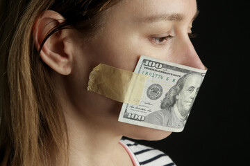 Money buys silence. Woman's mouth covered with dollar bill. Corruption and freedom of speech concept.
