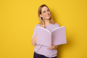 Young smiling woman making notes in a notebook smiling against a yellow background.