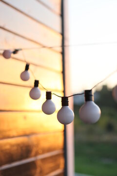 Garland of white light bulbs hanging on  wooden terrace in summer evening