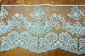 White textile lace with an ornament on a brown background. Top view. Decoration for clothes and fabrics.