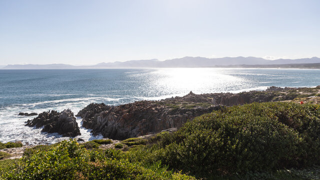 Die Sonne strahlt auf die wundervolle Bucht von Gansbaai an der Garden Route in S&uuml;dafrika, im Hintergrund ragt eine langgezogene Bergkette empor