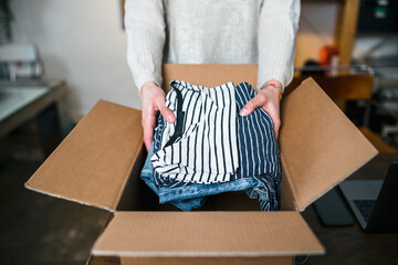 Business Woman prepares a package in a cardboard box for shipping with clothes from her online...