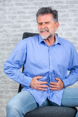 Mature man having a stomachache. Old male having strong abdominal ache, stomach ulcer disease, health problems. Businessman holding his stomach in pain.