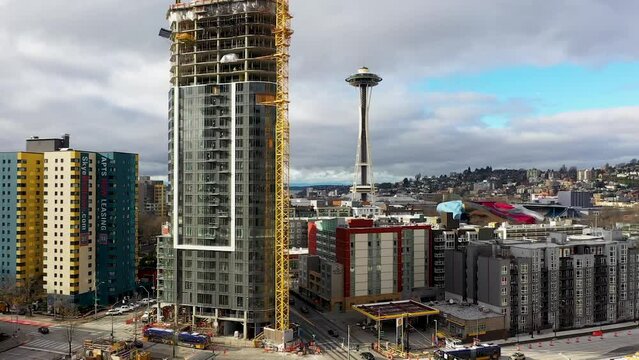 Descending aerial of a skyscraper under construction with the Space Needle in the background.