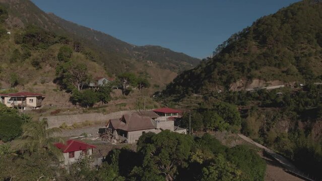 remote village town in mountainous tropical region Kabayan Benguet Philippines aerial fast approaching wide angle house on edge of valley blue sky sunny day