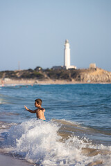 Funny kid enjoying the water of the ocean with a lighthouse background