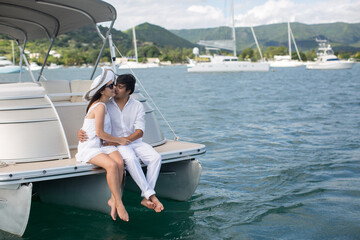 Young couple is traveling on a yacht in the Indian ocean. Man and a woman sit on the edge of the boat and kiss