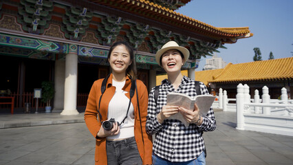 happy females walking with a tourist guide joyfully talking about the attractions in the distance near Buddhist temples they are visiting.