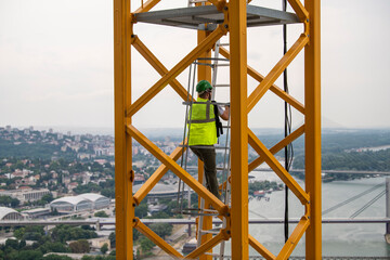 Crane operator climbing up yellow steel staircase, crane access ladder. Construction site of...