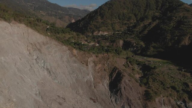 Village on the edge of a cliff in a mountainous region valley surrounded by trees aerial reversing revealing huge rock wall Kabayan Benguet Philippines