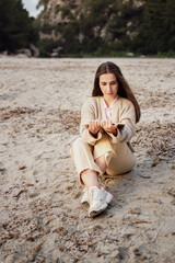 Woman sitting on the sand reading a book on a beach in spring clothes.