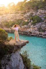 Traveller in a hat and bright clothes on a cliff enjoying her holiday on the crystal clear Mediterranean coast.