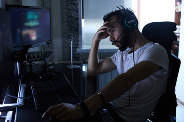 a young 30-year-old gamer is sitting at a computer, playing computer games, nervous, angry,...