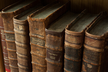 Dusty, worn and faded, leather-bound, large volume, antique Jewish holy books stacked upright on a...