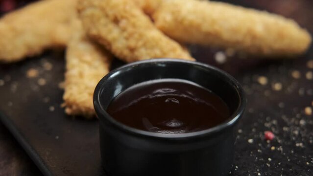 golden chicken strips.. fast food. american food. appetizing chicken lies on a plate with barbecue sauce. Slow motion. close-up. dark background