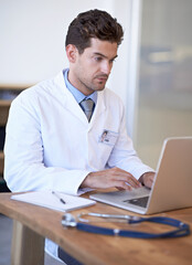 Well informed on every medical procedure. Shot of a young doctor at work on a laptop.