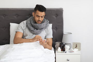 Sick Young Middle Eastern Man Sitting In Bed And Taking Medicine