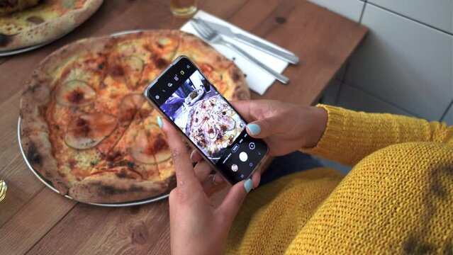 Video of close up woman hands photographing delicious pizza with her smart phone in a restaurant.